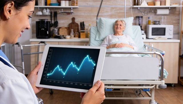 Nurse holding tablet showing rising health data chart beside elderly patient in bed