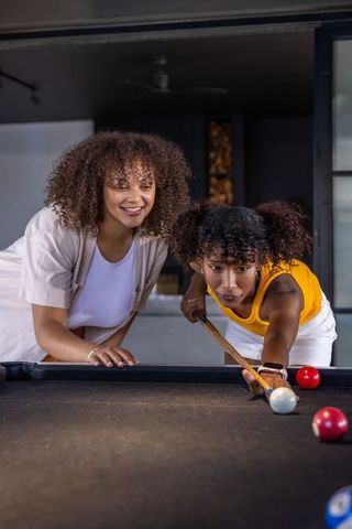 Friends playing pool in modern game room, woman aiming cue while friend watches and smiles