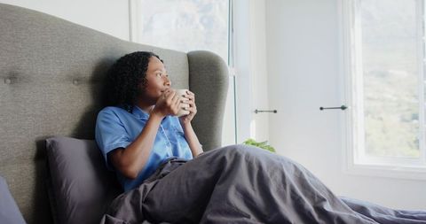 African american woman enjoying morning coffee in cozy sunlit bedroom