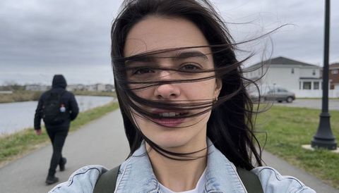 Windblown woman holding phone on suburban canal path wearing denim jacket