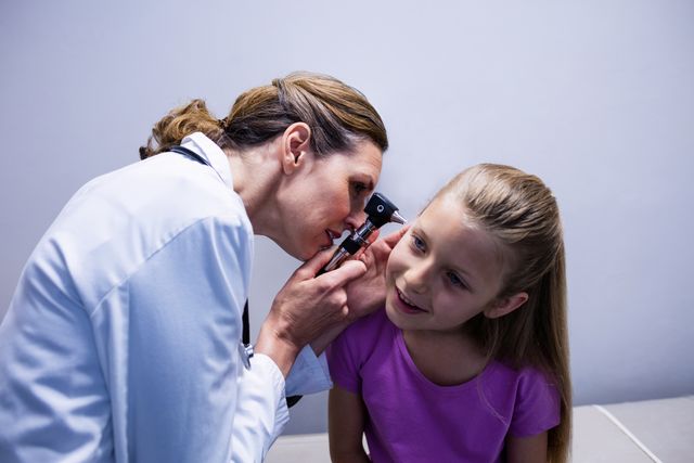 Female doctor examining young girl's ear with an otoscope. Ideal for use in healthcare, medical, and pediatric contexts. Can be used in articles, brochures, and websites related to child health, medical checkups, and healthcare services.