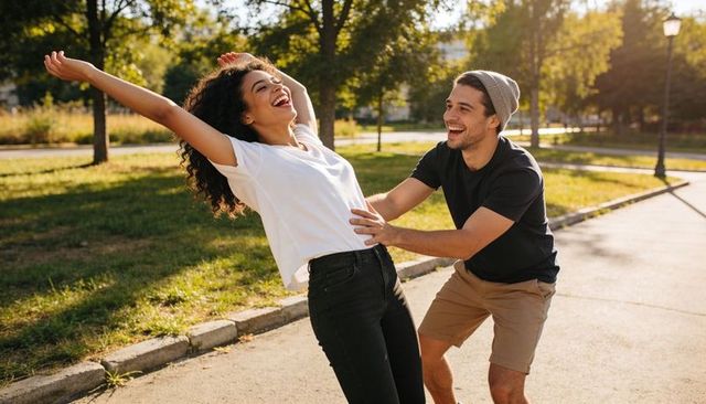 Playful couple enjoying sunny park, laughing woman leaning back while partner reaching