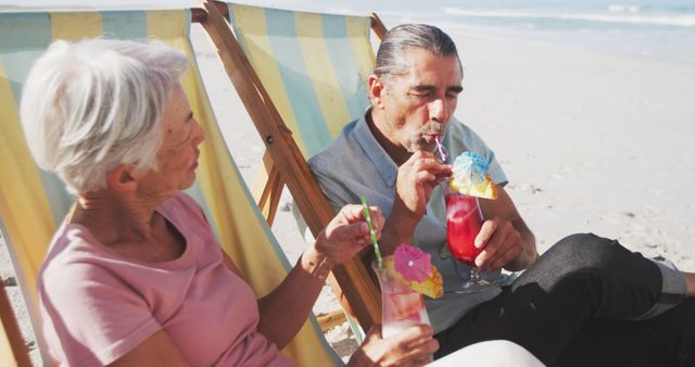 Happy senior caucasian couple sitting on deckchairs and drinking cocktails on beach. Senior lifestyle, realxation, nature, free time and vacation.