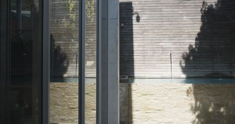 Sunlit minimalist courtyard with vertical glazing, concrete column, narrow reflecting pool