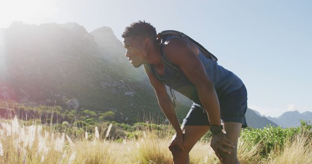 African american man exercising outdoors leaning on his knees in countryside on a mountain. fitness training and healthy outdoor lifestyle.
