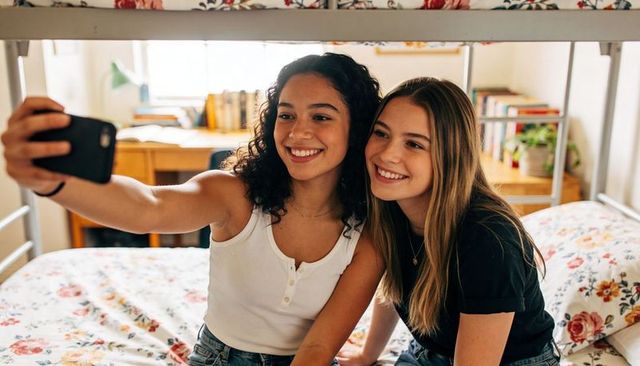 Teen friends taking selfie on bunk bed with floral bedding and cozy dorm decor