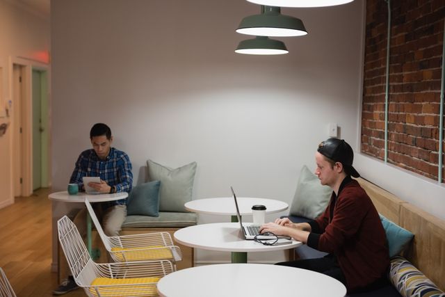 Young professionals working in a modern office lounge. One person is using a laptop while another is using a tablet. Ideal for illustrating coworking spaces, modern work environments, and technology in business settings.