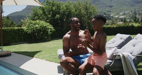 Father and son laughing and splashing poolside on sunny backyard summer day