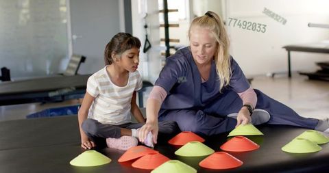 Clinician in navy scrubs guiding child through coordination drill with colorful cones