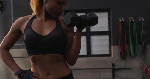 Woman performing bicep curl with dumbbell in modern gym