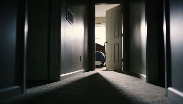 Sunlit bedroom doorway casting dramatic triangle of light down quiet hallway