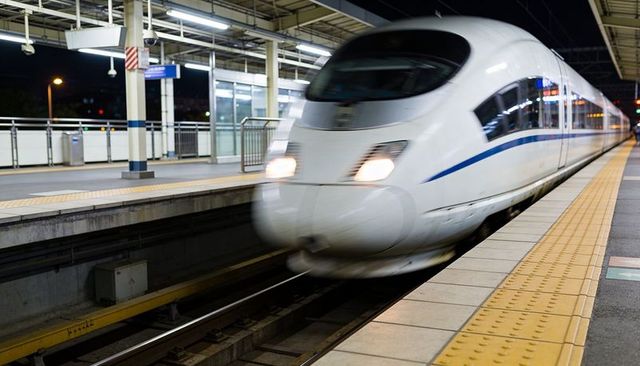 High-speed bullet train passing illuminated platform at night with motion blur and yellow paving
