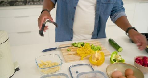 Man chopping yellow bell pepper and cucumber on cutting board in modern white kitchen