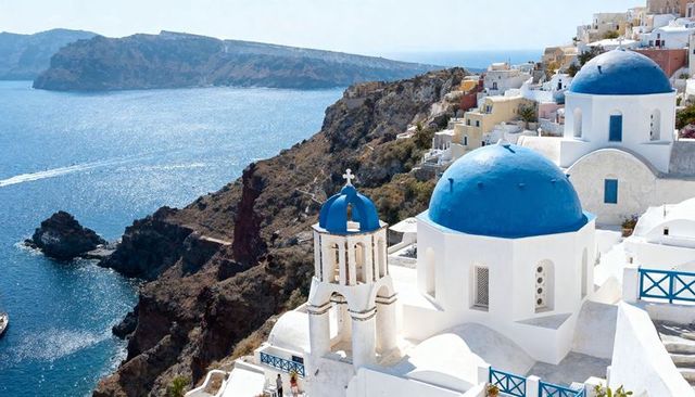 Sunlit santorini blue domes and bell tower overlooking aegean caldera on cliffside