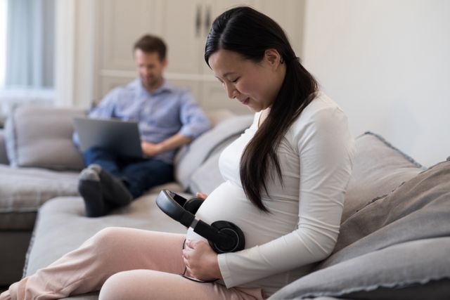 Pregnant woman placing headphones on her stomach at home