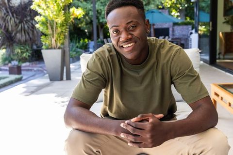 Smiling african american man relaxing on sunlit patio couch wearing olive t-shirt