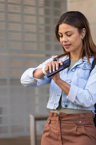 African american woman tapping smartphone wearing denim jacket, smartwatch on city commute