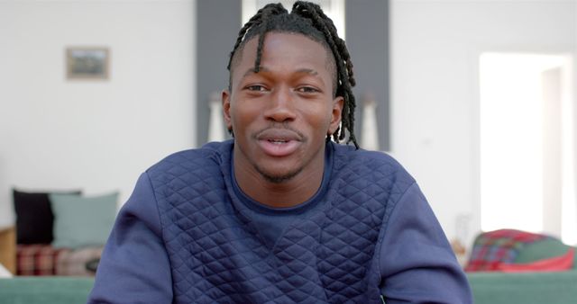 Young man with dreadlocks is talking to the camera in a casual home environment. Useful for content about modern lifestyle, home videos, personal vlogs, and friendly conversations.