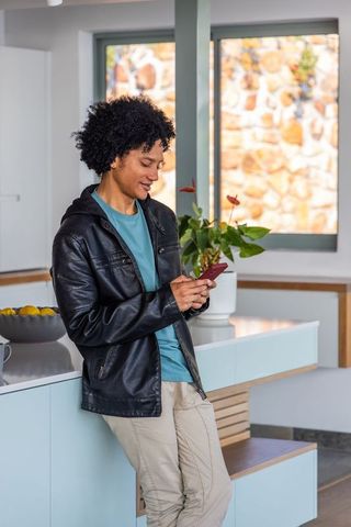 Young african american man leaning on kitchen island texting on smartphone in modern home