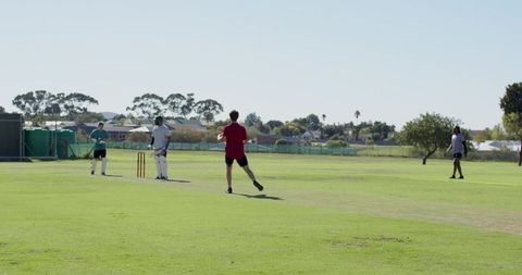 Bowler running toward crease on suburban cricket pitch during sunny practice session
