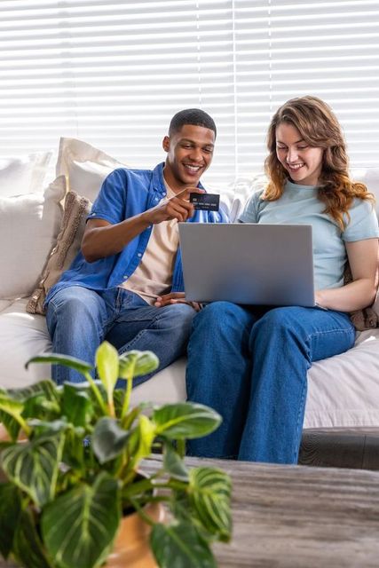 Young couple shopping online with credit card on cozy living room sofa