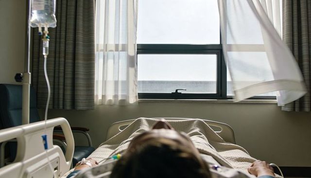 Patient lying on hospital bed receiving iv and cardiac monitoring with daylight window view