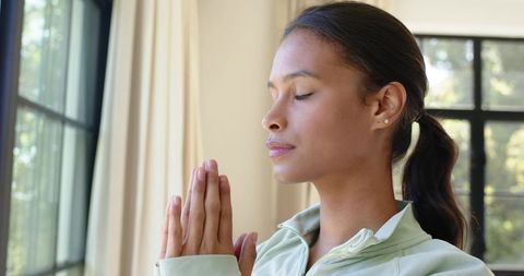 African american woman meditating by window practicing mindfulness and calm