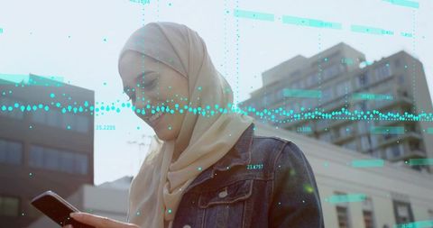 Young muslim woman using smartphone with turquoise data overlay in modern city daylight