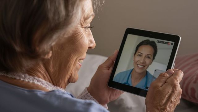 Senior woman smiling holding tablet consulting doctor via telehealth video call at home