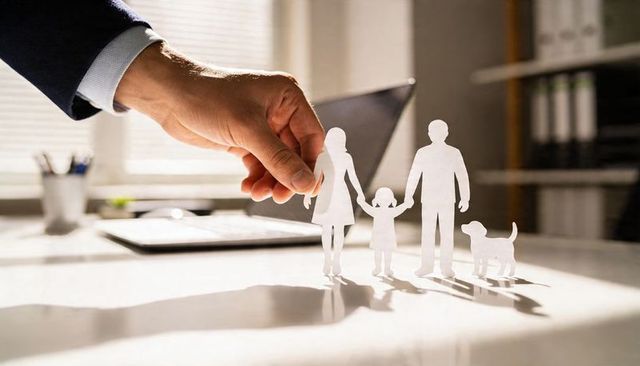 Business hand placing paper family cutouts on office desk representing insurance protection