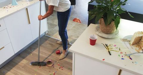 Woman Sweeping Messy Kitchen After Birthday Celebration