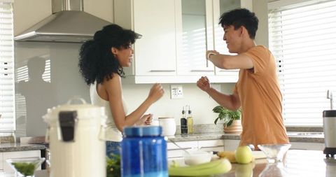 Multiracial Couple Laughing and Dancing in Bright Kitchen While Preparing Breakfast