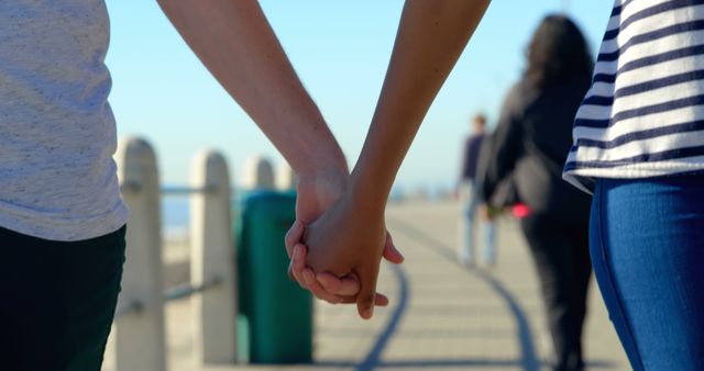 Two people are holding hands, suggesting a close relationship or friendship, with copy space. Their casual attire and the outdoor setting imply a relaxed, leisurely atmosphere.
