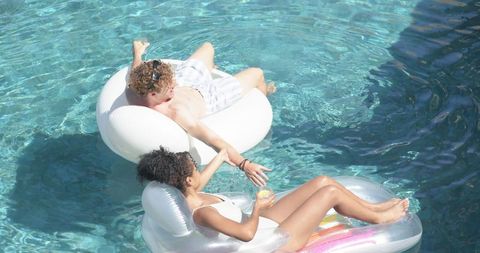 Young couple relaxing on pool floats holding hands enjoying summer sun and drinks