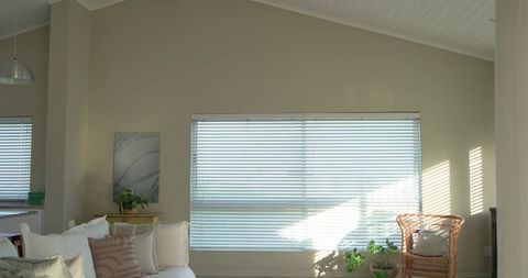 Sunlit living room with blinds casting slatted shadows on sofa and rattan chair