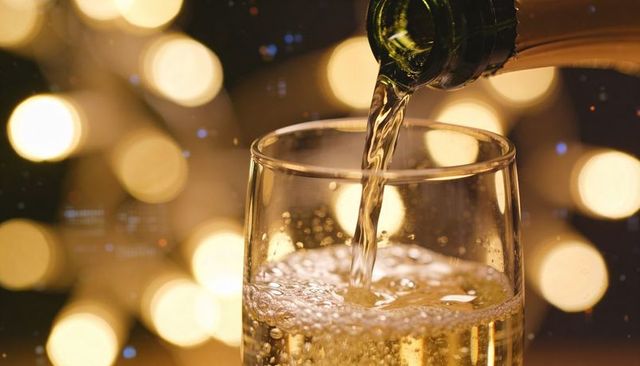 Pouring sparkling wine into glass with golden bubbles and festive bokeh lights celebration ambience