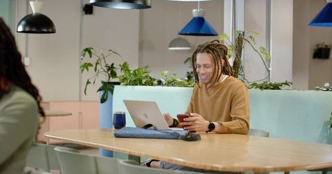 African American man smiling while working at communal coworking table with laptop and phone