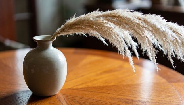 Beige ceramic vase with pampas grass on round wood table minimalist neutral still life