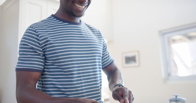 Man standing in a contemporary kitchen chopping or preparing food, looking happy and focused. Ideal for use in content related to home cooking, healthy eating, domestic life, or promoting kitchen appliances and accessories. Can be used in lifestyle blogs, websites, or advertisements encouraging home cooking and joyful living.