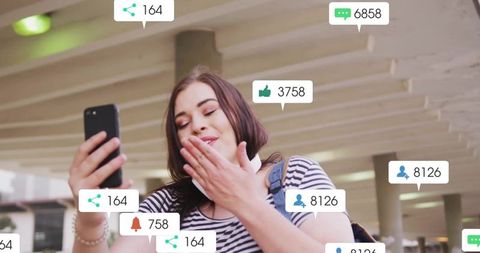 Smiling woman blowing kiss holding smartphone with social media notification overlays