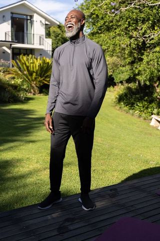 Senior african american man laughing on deck outside modern home in casual activewear