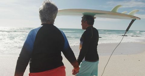 Senior Couple Walking on Beach with Surfboard During Retirement