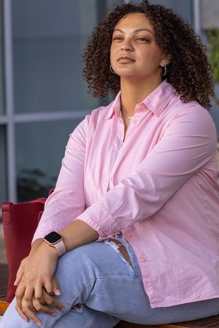 Contemplative african american woman sitting in pink shirt and ripped jeans near plaza urban