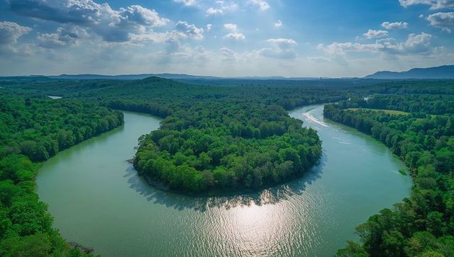 Winding river meander curving around forested peninsula with sunlight reflection