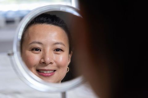 Mature asian woman smiling in round mirror wearing gold hoop earrings closeup beauty soft