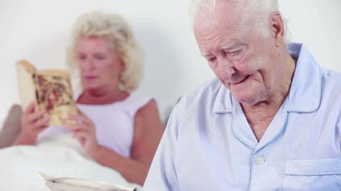 Elderly Couple Reading Books and Newspapers in Shared Bedroom