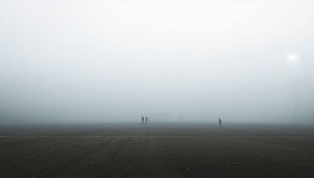Standing silhouettes near soccer goal on foggy pitch with lone floodlight glow
