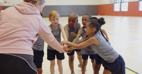 Youth basketball team huddling with coach on gym court