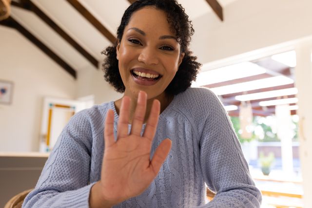 Happy biracial woman making video call, waving and smiling to camera at home, with copy space. Inclusivity, domestic life, leisure time and communication concept.