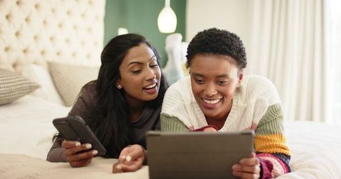 Diverse Female Friends Relaxing and Using Gadgets on Bed